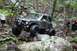 1984 Ford Bronco II - An off-road SUV tackles a rocky trail in a wooded area, with another vehicle visible in the background.