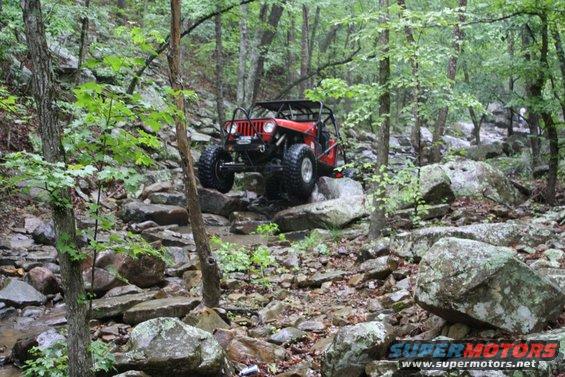 Red off-road vehicle with roll cage climbing over rocks