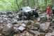 1984 Ford Bronco II - Two off-road vehicles traverse a challenging rocky path in a forest setting.
