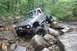 1984 Ford Bronco II - A modified off-road vehicle tackles a challenging rocky trail in a forest setting.