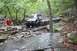 1984 Ford Bronco II - Two off-road vehicles tackle a challenging, rocky path in a wooded area.