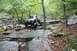 1984 Ford Bronco II - A modified off-road vehicle tackles a challenging rocky terrain in a wooded area.