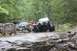 1984 Ford Bronco II - A modified 1984 Ford Bronco II tackles a challenging rocky obstacle on an off-road trail, with another vehicle visible in the background.