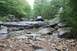 1984 Ford Bronco II - Off-road vehicle navigating a challenging rocky path in a wooded area.