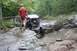 1984 Ford Bronco II - A person in a red shirt watches an off-road buggy traverse a challenging, water-filled rocky path.