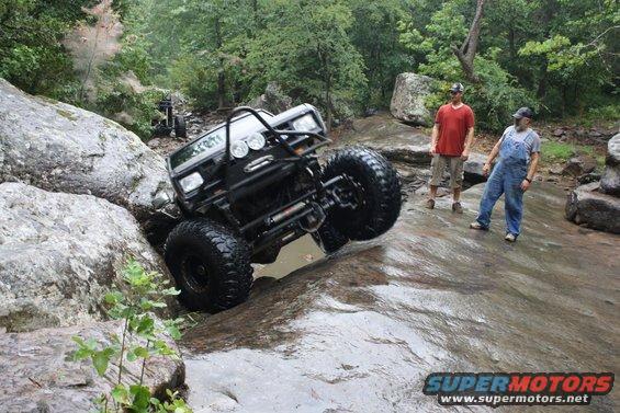Modified off-road vehicle climbing rocks with two men watching