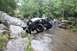 1984 Ford Bronco II - A person observes a custom off-road vehicle as it maneuvers through a challenging rocky stream environment.