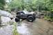 1984 Ford Bronco II - An off-road SUV with oversized tires climbs over a large rock in a wooded stream environment.