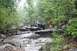 1984 Ford Bronco II - A person directs an off-road vehicle through a challenging rocky terrain with a stream.