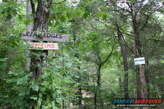 Wooden signs on trees reading 'JEFF LEDGES' and '5 T5CLIMB' in a wooded area