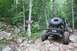 1984 Ford Bronco II - Off-road vehicle tackles a challenging rocky path in a wooded area. Signage indicates a trail.