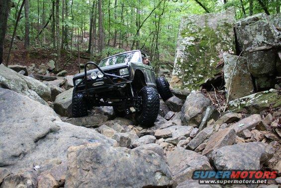 Green off-road SUV with large tires climbing over rocks