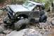 1984 Ford Bronco II - A modified off-road vehicle is shown attempting to climb over large rocks on a wooded trail.