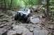 1984 Ford Bronco II - Modified SUV tackles a challenging rocky terrain in a wooded area.