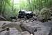 1984 Ford Bronco II - Off-road vehicle tackles a challenging rocky trail surrounded by dense forest foliage.