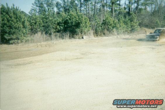 Pickup truck kicking up dust on a dirt road with trees in the background