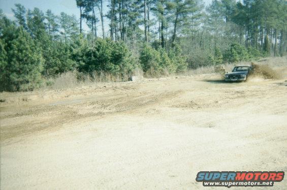 Dark pickup truck kicking up mud on a dirt track, 1970s era