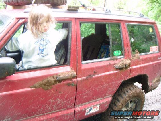 Red 1998 Jeep Cherokee side view with child in driver's seat, covered in mud
