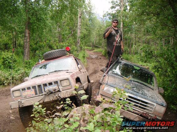1998 Jeep Cherokee and another SUV stuck on a muddy trail with a person standing on the second vehicle