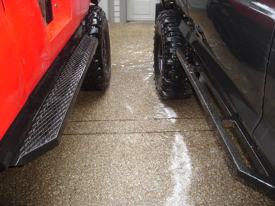 Side view of a red off-road vehicle next to a black off-road vehicle, both with large tires and running boards