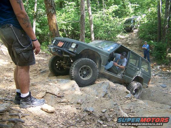 Green Jeep Cherokee XJ off-roading on a rocky incline, driver visible