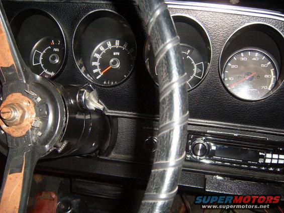 Close-up of a car's dashboard with fuel and speed gauges, a steering wheel, and a radio