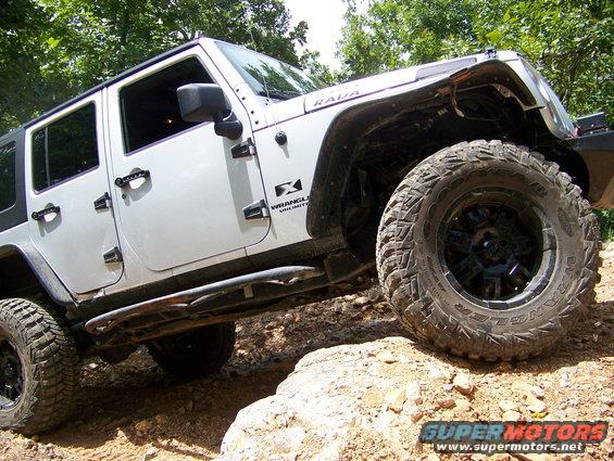 White Jeep Wrangler Unlimited with off-road tires climbing rocks
