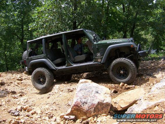 Green Jeep Wrangler Sahara driving over rocks on a trail. Doors are off