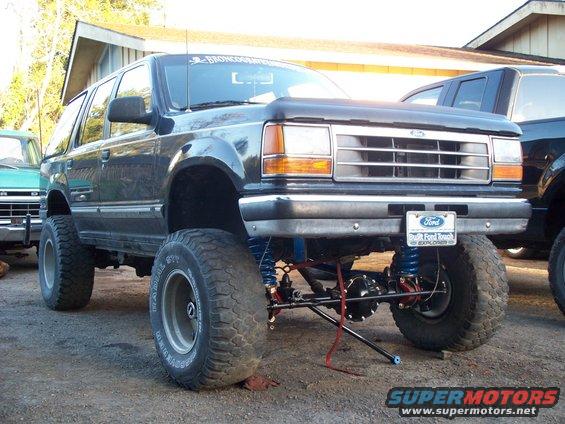 Lifted first-generation Ford Explorer with large tires and suspension modifications. Another vehicle is partially visible to the left