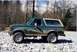 1990 Ford Bronco - Side view of a green 1990 Ford Bronco parked on a rocky terrain with a wooded area behind it.