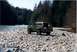 1990 Ford Bronco - 1990 Ford Bronco parked on a rocky shore next to a flowing river, with a dense forest in the background.
