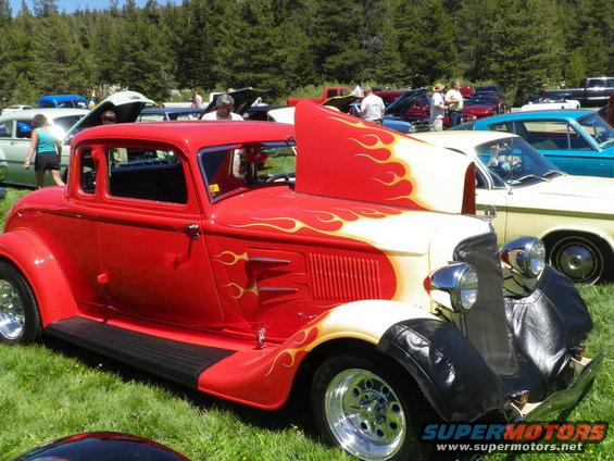 Red coupe hot rod with yellow and orange flames on hood and fenders, black running boards, chrome wheels