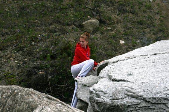 Woman in red hoodie and grey pants crouches on large rocks