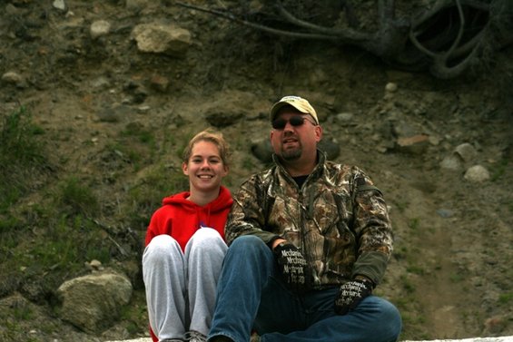 Man in camouflage jacket and girl in red hoodie sit outside