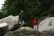 1990 Chevrolet Suburban - Two people explore a rocky area with dense trees in the background.