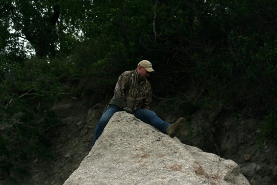 Man in camouflage sitting on a large rock outdoors