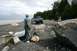 1990 Chevrolet Suburban - A light blue 1990 Chevrolet Suburban is parked on a rocky beach near the water, with a person standing nearby.