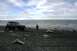 1990 Chevrolet Suburban - A teal SUV sits on a dark, rocky shore with a person walking away from it towards the water.