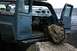 1990 Chevrolet Suburban - A blue van sits on a rocky shore with its doors open, facing the ocean.