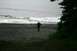 1990 Chevrolet Suburban - A lone figure stands on a pebble beach as waves crash ashore under an overcast sky.