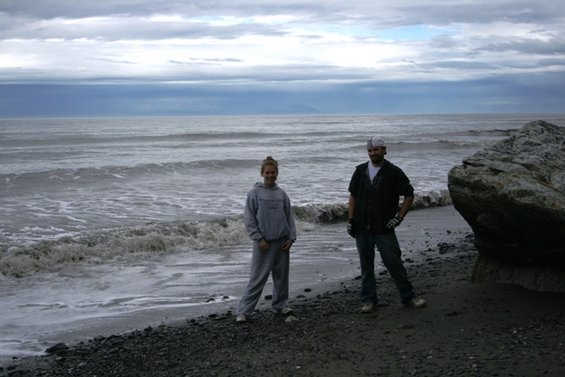 Two people stand on a rocky beach with waves crashing