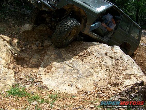 Green Jeep Cherokee XJ off-roading over rocks, driver visible inside
