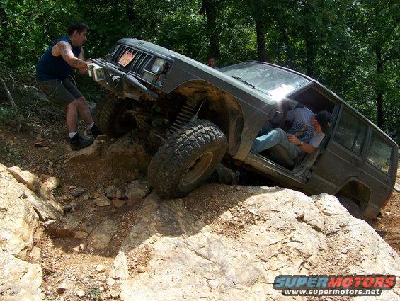 Jeep Cherokee XJ with open doors on rocky terrain, one person pushing