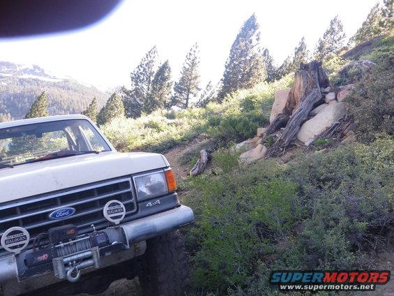 Ford F-Series truck with winch on a dirt road, mountains and trees in background
