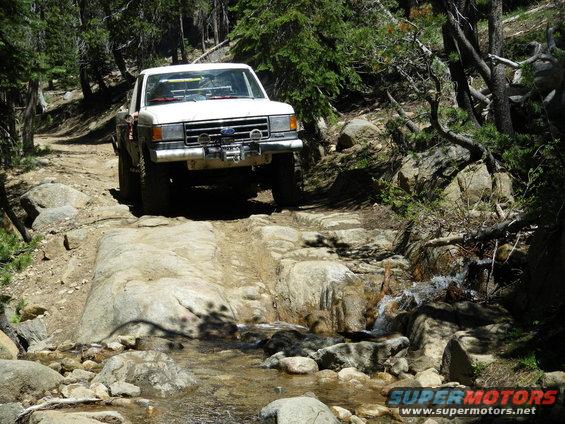 White Ford F-Series truck driving over rocks and through a stream on a dirt trail