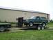 1989 Ford Bronco - A green Ford Bronco is being transported on a trailer, parked in front of a large industrial building.
