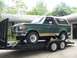 1989 Ford Bronco - A green 1987 Ford Bronco is loaded onto a trailer, showing its front-left side with tan trim and white wheels.
