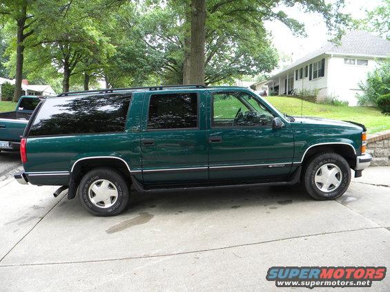 Green 1999 Chevrolet Suburban parked on driveway, with a pickup truck behind it