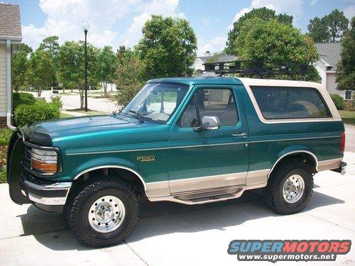 Green and tan Ford Bronco with a roof rack and brush guard parked in a driveway