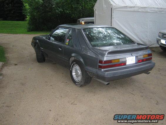 Gray 1985 Ford Mustang hatchback with a spoiler and aftermarket wheels parked on a dirt lot